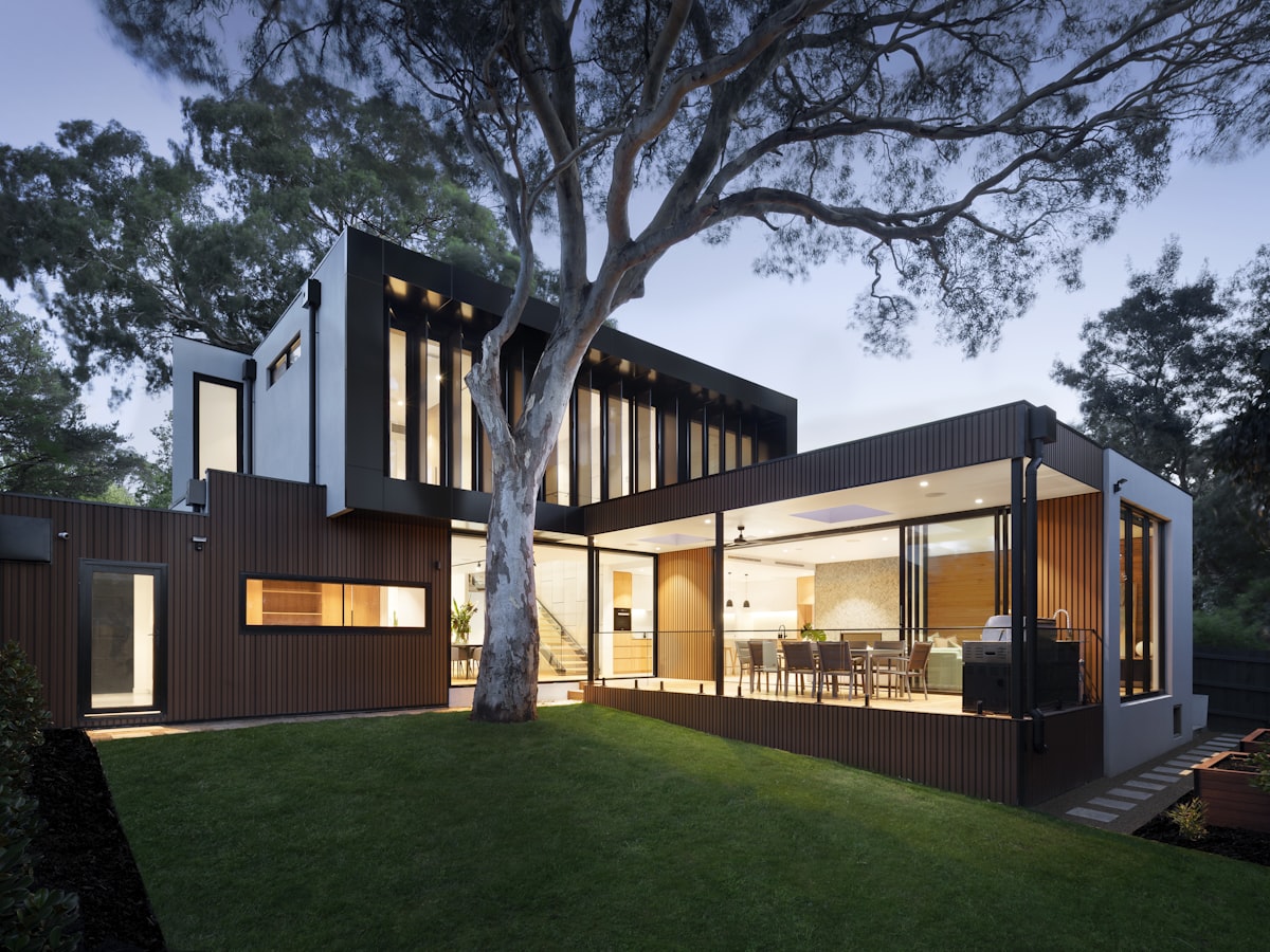 A modern home at dusk with a manicured lawn and mature shade tree